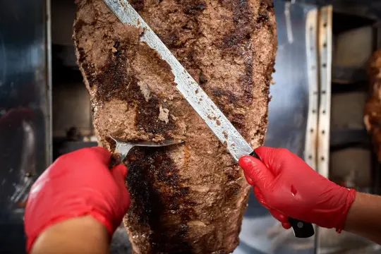 Ręce w czerwonych rękawiczkach kroją soczyste mięso z pionowego rożna. To początek przygotowania pysznego, aromatycznego kebab.