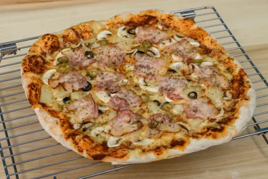 Pyszna pizza z szynką, pieczarkami i oliwkami, idealna do pieczenia w piekarniku.
